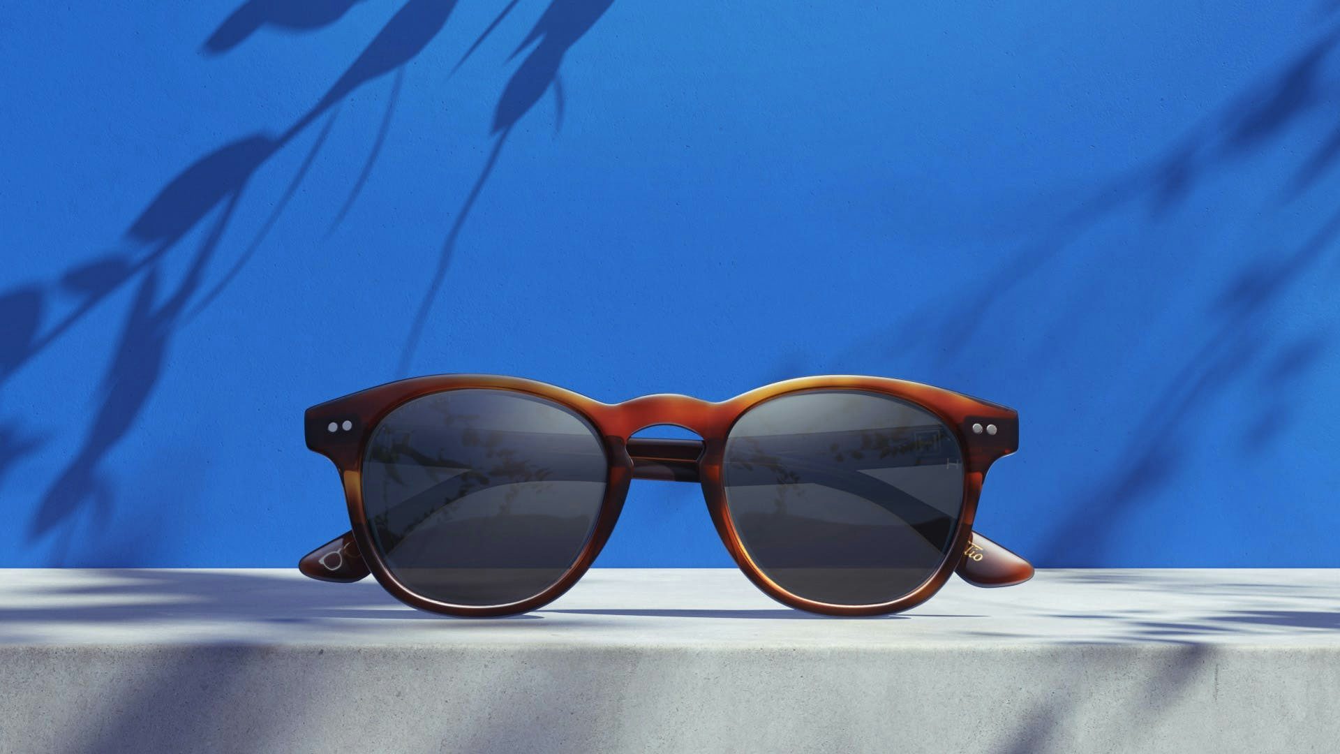 A pair of sunglasses on top of a stone surface with a blue background. Shadows from branches all over.
